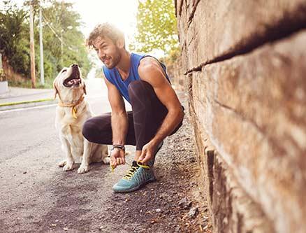 man ties shoe with dog at his side